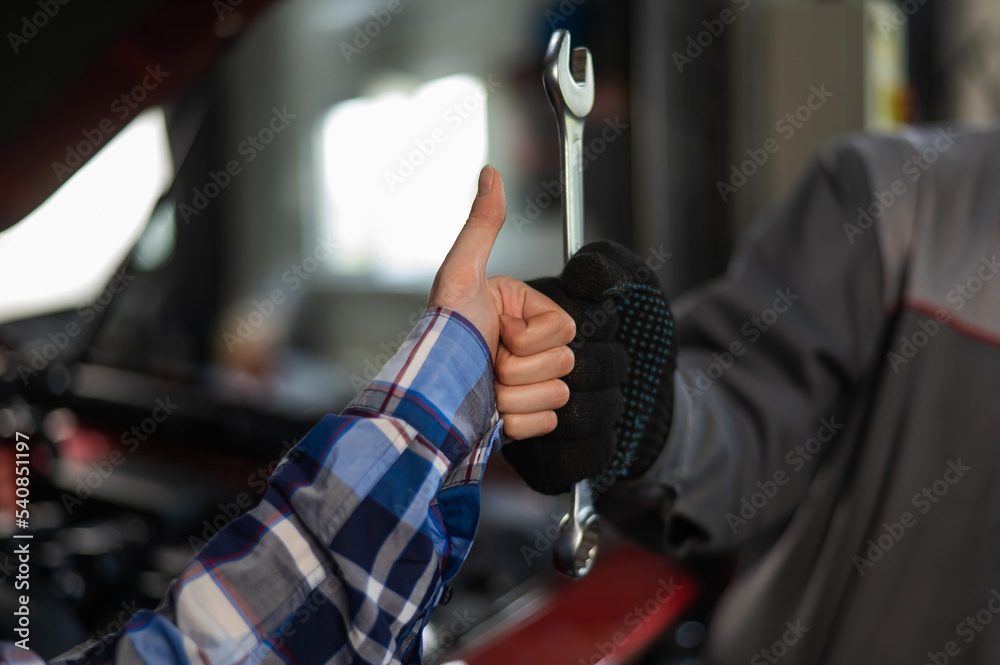 Close-up of woman's hand thumb up and mechanic's hand with tool. Automotive master in gloves shows a positive gesture after finishing work