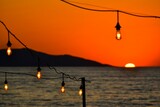 Bulbs hanging from wires with the ocean and a beautiful sunset sky in the background.