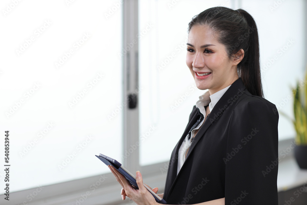 Portrait of confident and beautiful young asian businesswoman with happy emotion standing and using tablet in modern office. Success business concept Portrait of confident and beautiful young asian businesswoman with happy emotion standing and using tablet in modern office. Success business concept