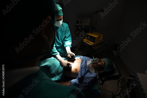 Closeup image of professional concentrated surgical team performing CPR with defibrillator on patient in hospital operating room or emergency room. Surgery concept