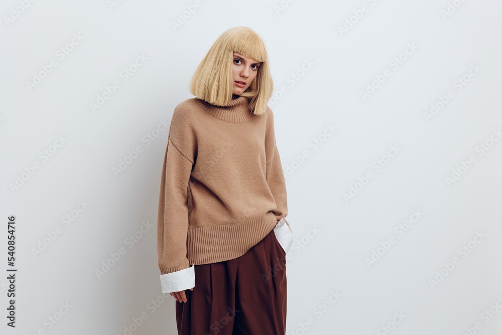 Fototapeta premium Horizontal photo, a woman on a white background in a beige sweater and brown trousers with beautiful blond hair is standing