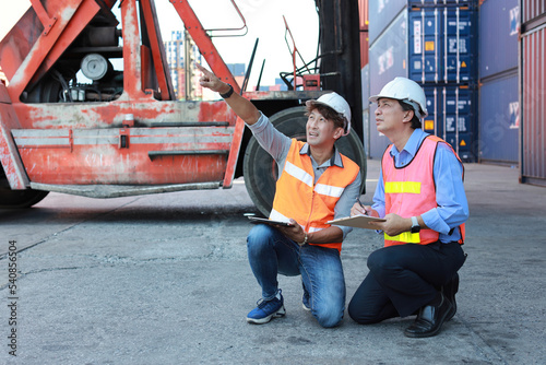 Asian architect men and worker sitting and checking large container with tablet and clipboard while pointing something. Engineer business manager looking in future with warehouse building.