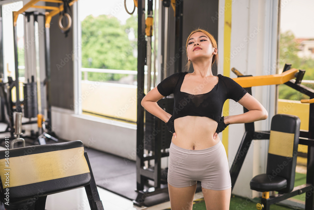 Fototapeta premium Candid scene of a young asian woman checking her figure while warming up at the gym.