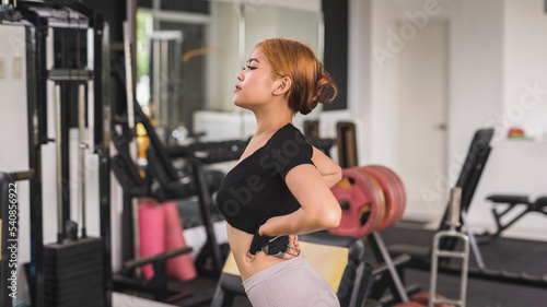Candid scene of a young asian woman checking her figure while warming up at the gym.