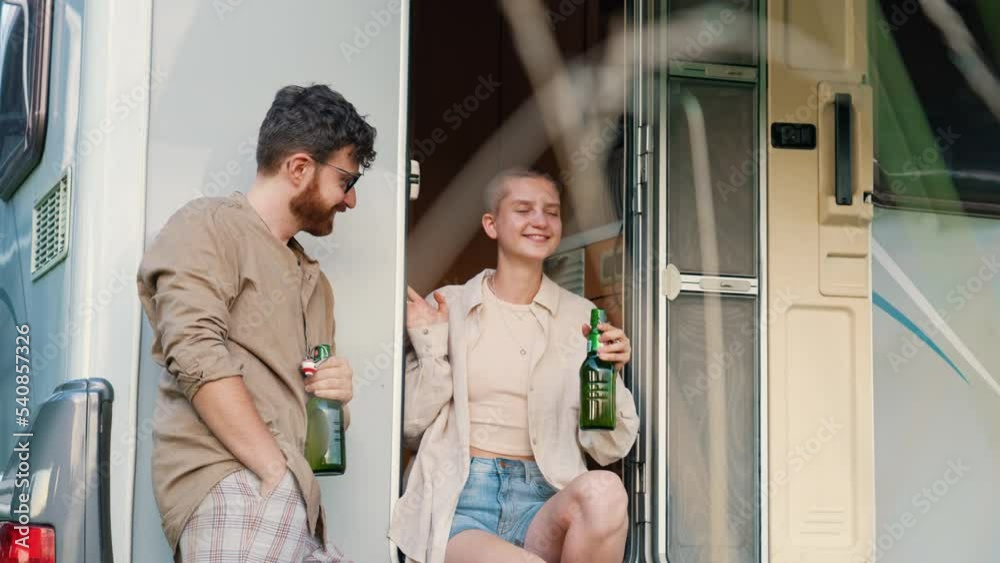Two young adult friends standing outside camper van door cheering with beer bottles then enjoying the view. Camping. Horizontal outdoor video. High quality 4k footage Two young adult friends standing outside camper van door cheering with beer bottles then enjoying the view. Camping. Horizontal outdoor video. High quality 4k footage