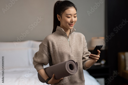 Young woman holding yoga mat and smartphone