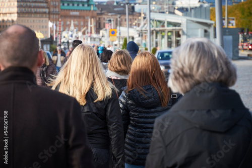 The focus is on two girls from the back while walking in a crowd in a city