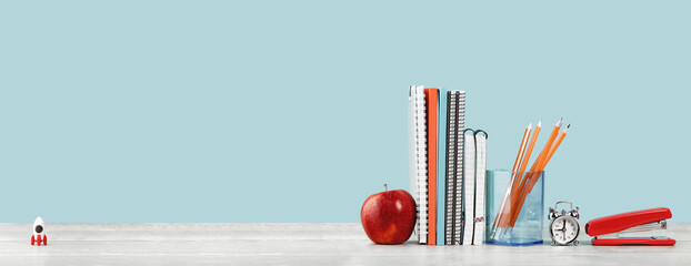 Organized office and school orange and pastel blue stationery, notebooks pencils scissors and alarm clock with red apple on grey wooden desk. Copy space for back to school education and craft concept