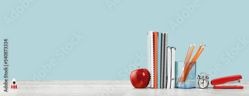 Organized office and school orange and pastel blue stationery, notebooks pencils scissors and alarm clock with red apple on grey wooden desk. Copy space for back to school education and craft concept