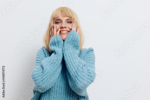 a happy, smiling woman stands on a light background and holds her hands on her cheeks, closing her eyes with delight. Horizontal photo