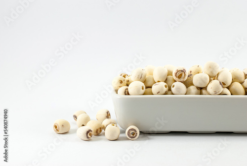 Dried lotus seeds are housed in white ceramic vessels and placed on a white background with copy space. photo