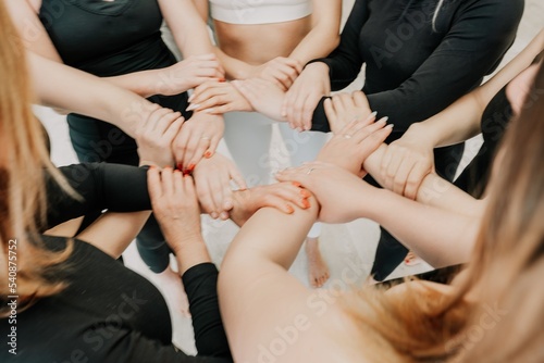 Partnership and unity concept: unrecognizable women in sportswear holding wrists of each other, forming circle. Group of happy young womans holding hands. Side view on human hands. Selective focus