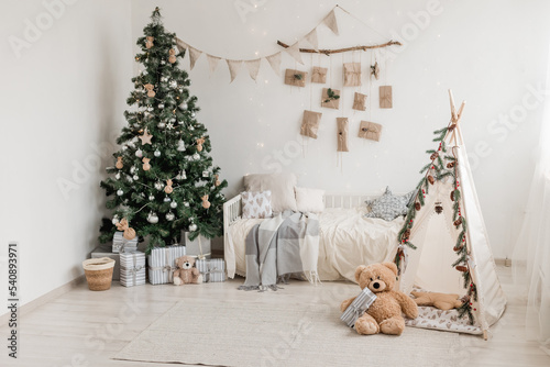New year 2023 american interior. children's tent decorated with spruce branches, cozy bed and Christmas tree decorated in beige natural colors. Advent calendar on the wall. selective focus
