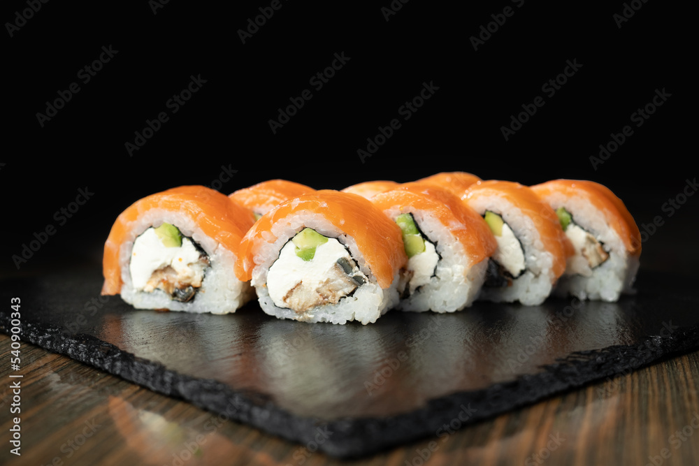 Sushi roll with salmon, smoked eel, avocado, cream cheese on black background. Sushi menu. Japanese food.