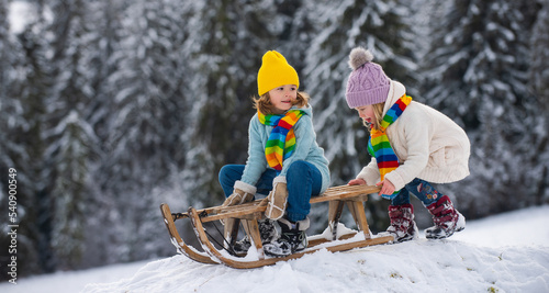 Happy kids having fun and riding the sledge in the winter snowy forest. Winter Christmas holidays and active winter weekend, children activities.