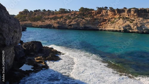 View of turquoise crystal clear sea with swinging waves and rocky coast in Mallorca island, Spain.