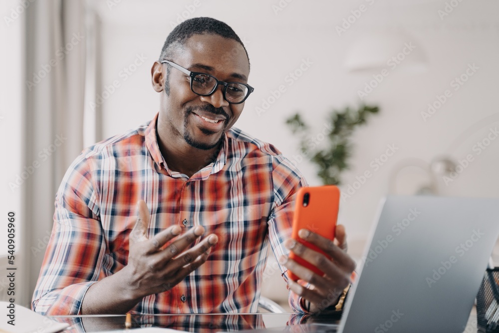 African american man in glasses talking online by video call, holding smartphone, using mobile apps African american man in glasses talking online by video call, holding smartphone, using mobile apps