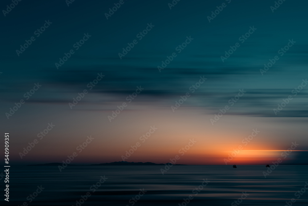 A sunset romantically caressing the silhouette of the island of Elba, admired from two boats drifting towards the horizon.  The observer loses himself in this natural picture and breathes in the calm 
