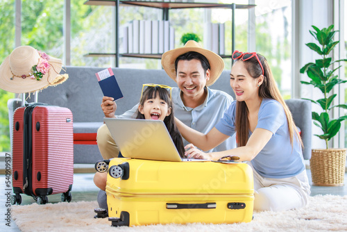 Millennial Asian lovely happy family father mother and young little girl daughter helping packing stuff in trolley luggage preparing to travel on summer vacation reserving hotel and airplane ticket