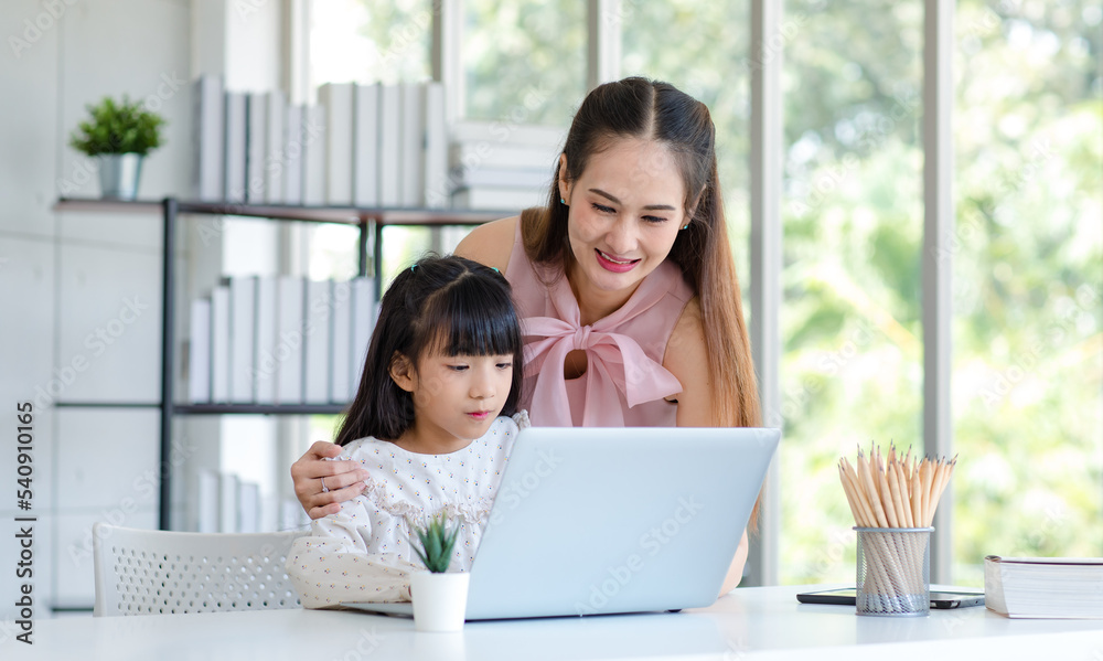 Millennial Asian happy family mother smiling helping supporting teaching little girl kid daughter studying learning doing online school homework via laptop notebook computer in living room at home Millennial Asian happy family mother smiling helping supporting teaching little girl kid daughter studying learning doing online school homework via laptop notebook computer in living room at home