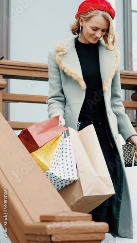 Young attractive woman walks with shopping bags in the old city. Female in coat and beret walking in autumn sunny day. Glamour blond lady.