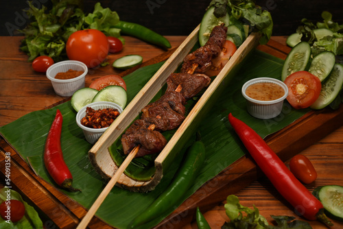 Appetizing grilled meat skewers in bamboo barrel plate and vegetables served on wooden board