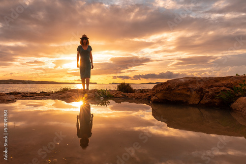 Sunset in Ibiza on vacation, a young woman walking by the sea in San Antonio Abad. Balearic