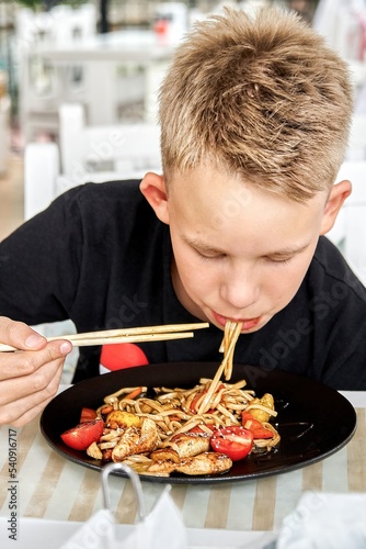 Junior schoolboy enjoys eating noodles with vegetables and spending summer holidays in resort town. Light-haired guy explores Asian culture in cafe