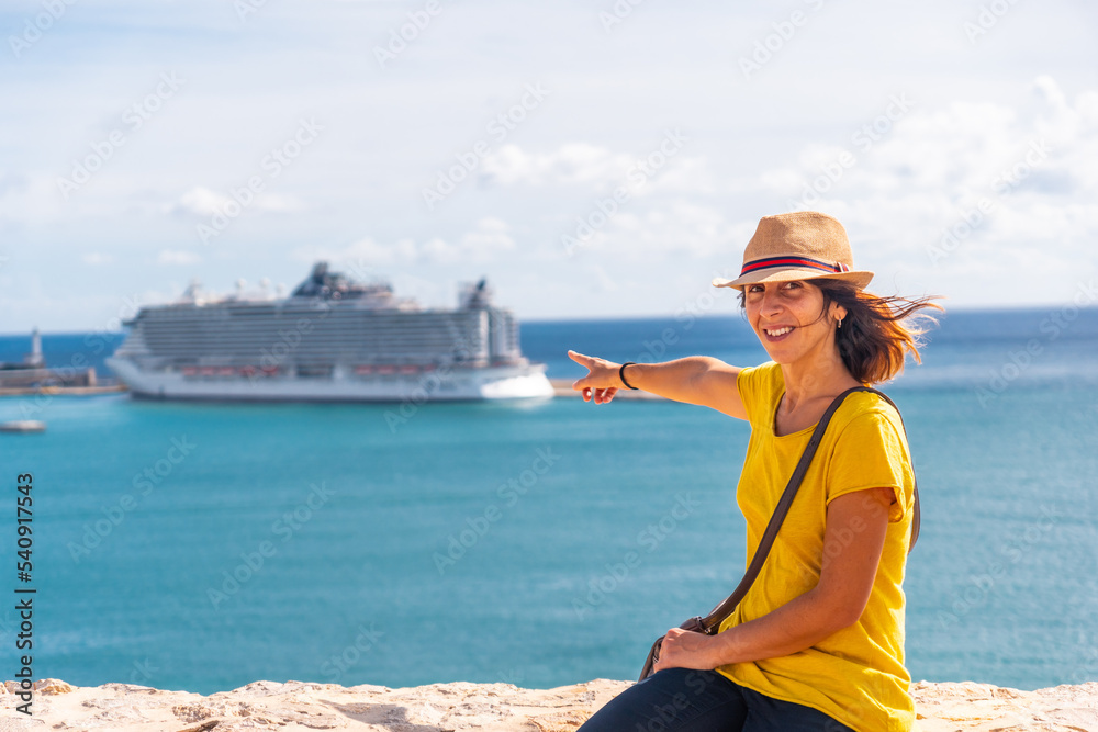 A young woman pointing on the cruise ship that she has arrived at the island of Ibiza to spend the holidays