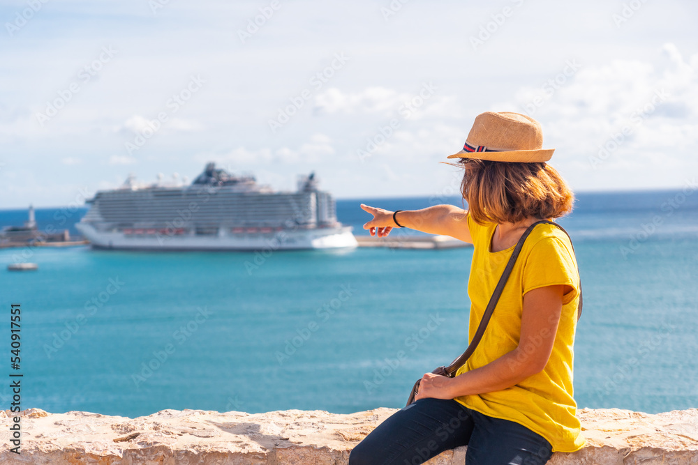 A young woman pointing at the cruise ship that has arrived on the island of Ibiza from the castle wall, Balearic Islands, Eivissa