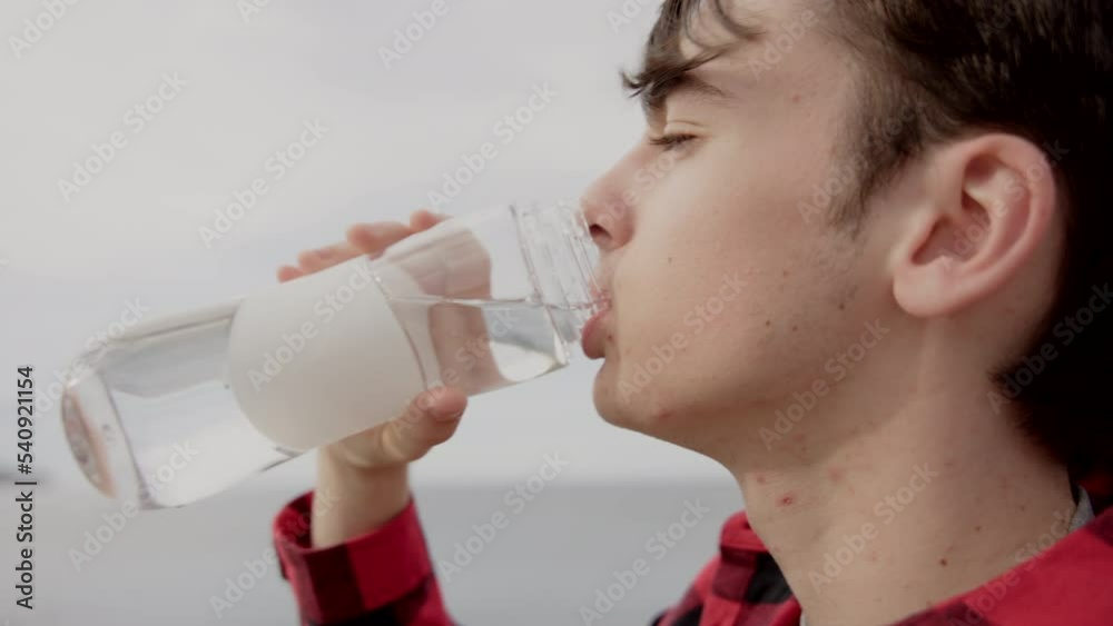 Teenager boy drinking water from a bottle outdoors at coastline Teenager boy drinking water from a bottle outdoors at coastline