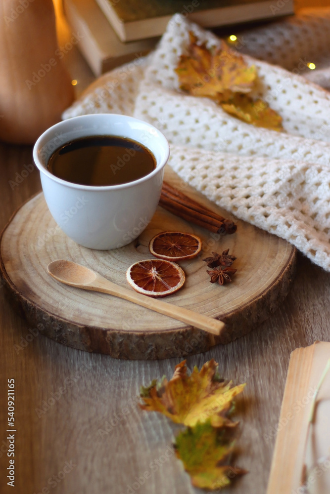 Fototapeta premium Cup of tea or coffee, seasonal spices, bowl of cookies, blanket, pumpkins, colorful leaves, books and tangerines on wooden table. Cozy hygge at home. Selective focus.
