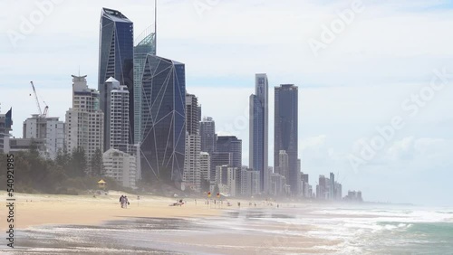 People walking on the golden sandy beach on a sunny day with high rise investment properties in the background, popular tourist destination in summer at Broadbeach Gold coast, Queensland, Australia. photo