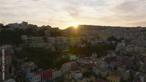 Colour multistorey apartment buildings in steep slope. Aerial view of urban borough against sun setting behind hill. Naples, Italy photo