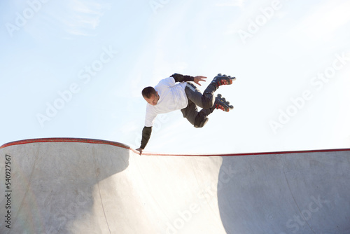 Energetic man on roller skates in motion at modern roller skate park. Roller skater doing dangerous and daring tricks. Sport, health, speed, and energy