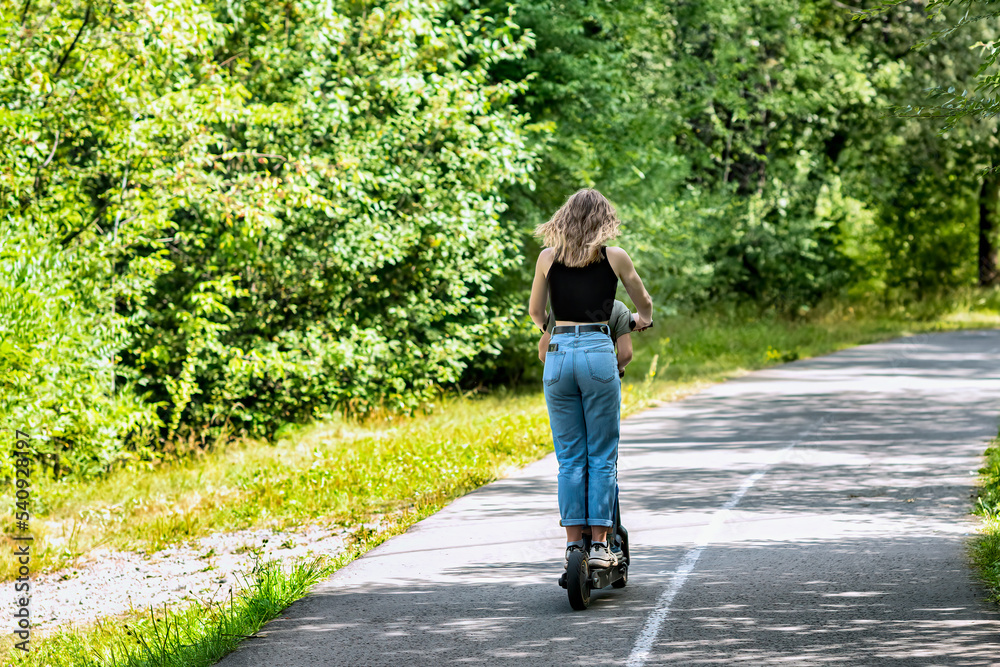 A young woman is riding on the electric scooter in a summer park. A young woman is riding on the electric scooter in a summer park.