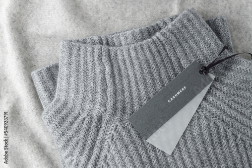 Soft textured sweater of grey luxury natural cashmere with blank paper tag lying on light wool background