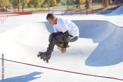 Energetic man on roller skates in motion at modern roller skate park. Roller skater doing dangerous and daring tricks. Sport, health, speed, and energy
