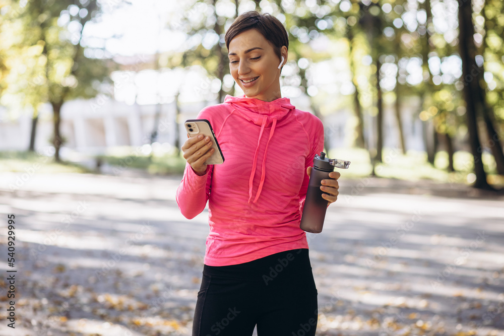 Sports woman using phone and drinking water in park Sports woman using phone and drinking water in park