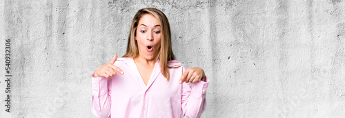 blonde adult woman feeling shocked, open-mouthed and amazed, looking and pointing downwards in disbelief and surprise photo