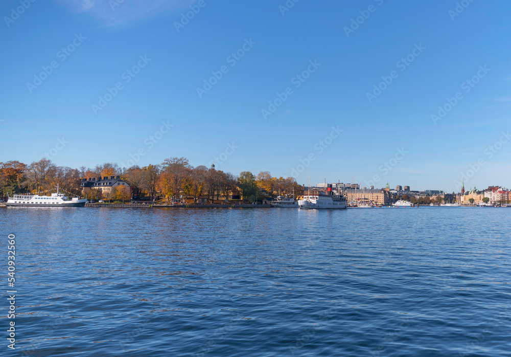 Panorama view, commuting steam boats and harbor ferries in the bay Ladugårdsviken with offices, apartment and hotel buildings a colorful autumn day in Stockholm