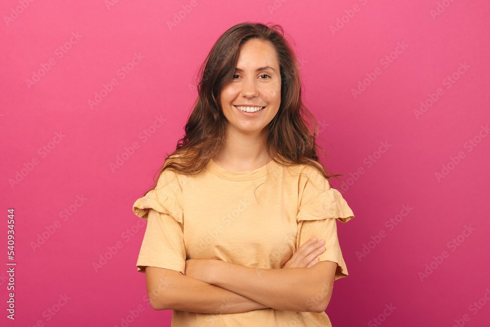 Portrait of young smiling woman standing over pink background with crossed arms and looking at camera. Portrait of young smiling woman standing over pink background with crossed arms and looking at camera.