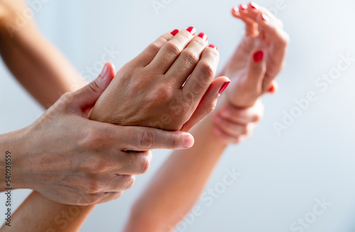 Masseuse holding a woman's beautiful hands with red nails, during a spa session.