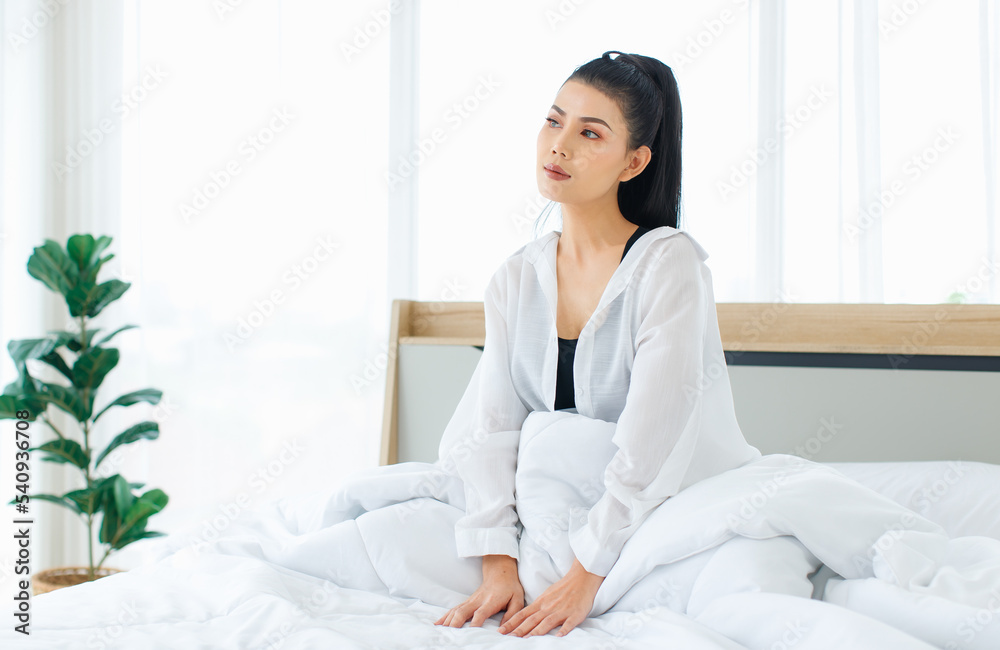 Millennial Asian sexy thoughtful female in casual comfort pajamas sitting under white thick warm blanket starting day thinking looking outside alone after waking up in bedroom in morning at home Millennial Asian sexy thoughtful female in casual comfort pajamas sitting under white thick warm blanket starting day thinking looking outside alone after waking up in bedroom in morning at home