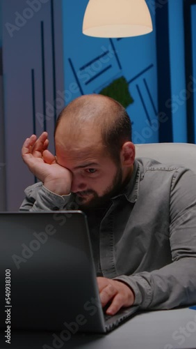 Exhausted sleppy businessman yawning while working at management project deadline late at night in start-up company office. Workaholic stressed entrepreneur typing financial strategy on laptop photo