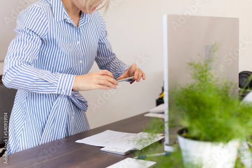 A woman works in the office, holds a phone in her hands and photographs documents.Business woman works at a computer at home or in the office.Work, office, online, freelance, remote work, business photo