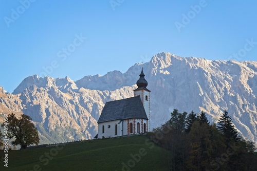 View of St. Nicholas Parish Church against the background of rocky mountains. Dienten, Austria. photo