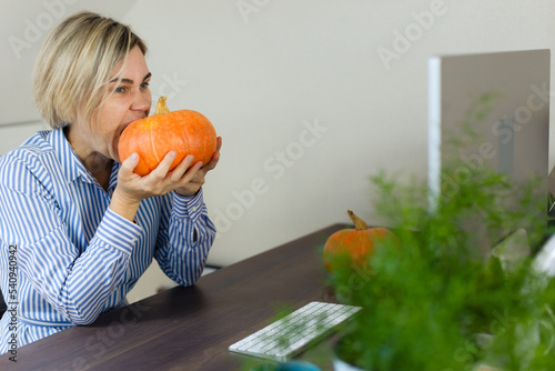 A female blogger is broadcasting, fooling around and biting a big orange pumpkin. Girl businessman working in the office, fooling around by video link. halloween, thanksgiving, autumn, pumpkin harvest