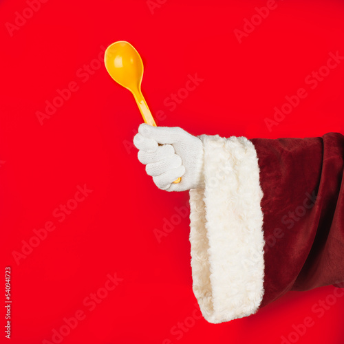 Santa Claus on holiday cooking. Santa Claus hand holding a plastic spoon on a red background. Kitchen and cooking concept.