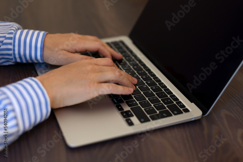 The girl is typing and working on a laptop.Keyboard and hands close-up on a wooden table. Work, business, print, laptop, search, information